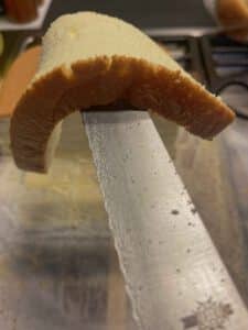 Een plak gesneden castella cake hang over een mes heen zonder te breken.